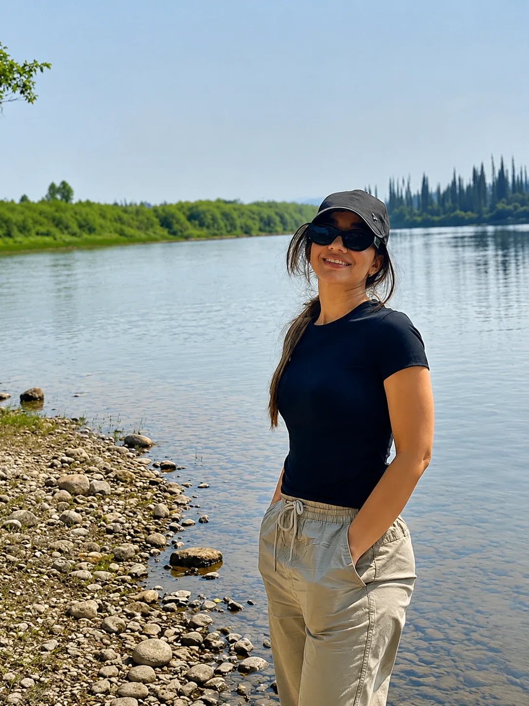 Behnoosh smiling beside a lake with a tree-lined shore