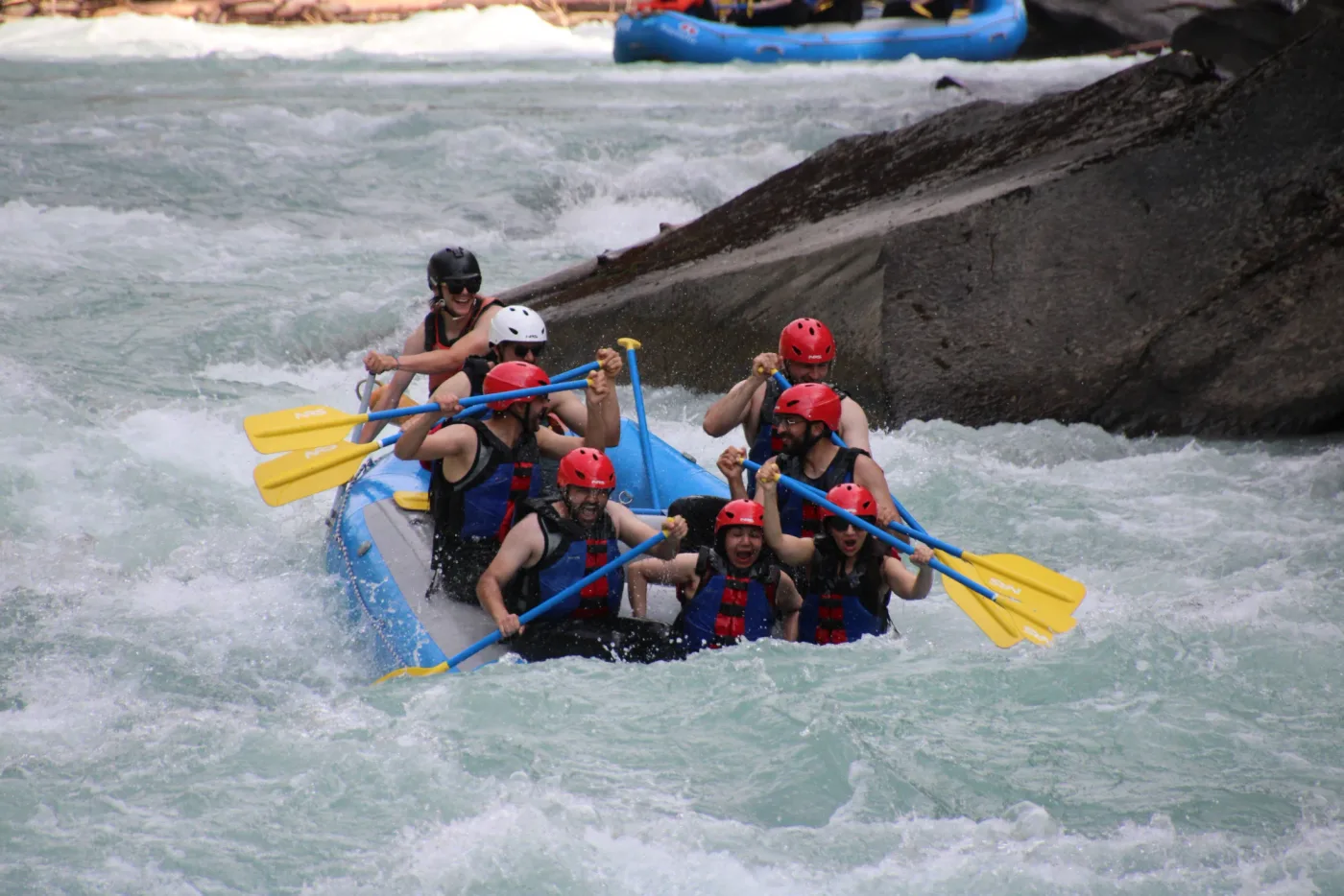 A blue raft carrying a group through foaming water.