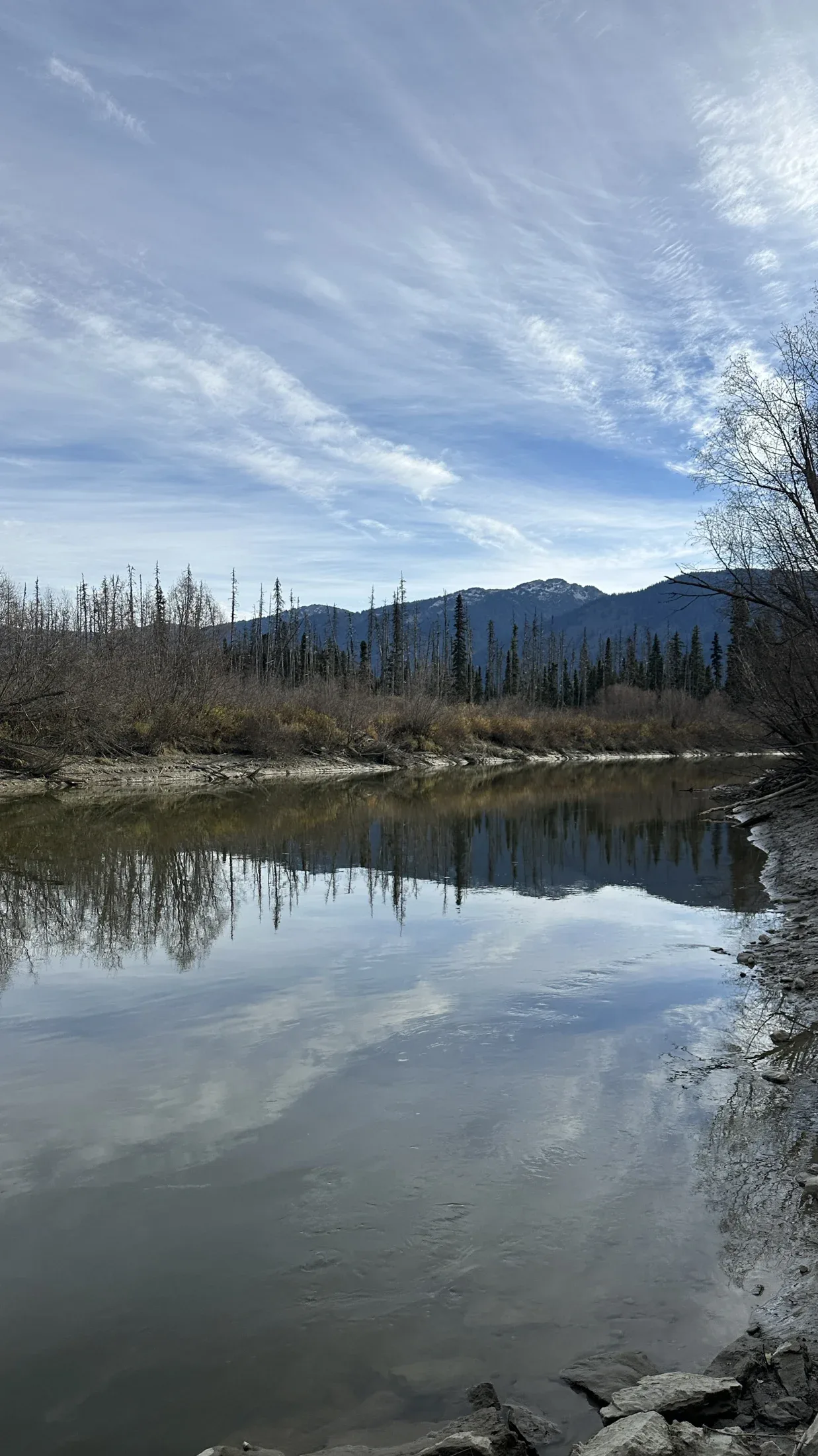 Clouds and wooded hills reflected in still water.